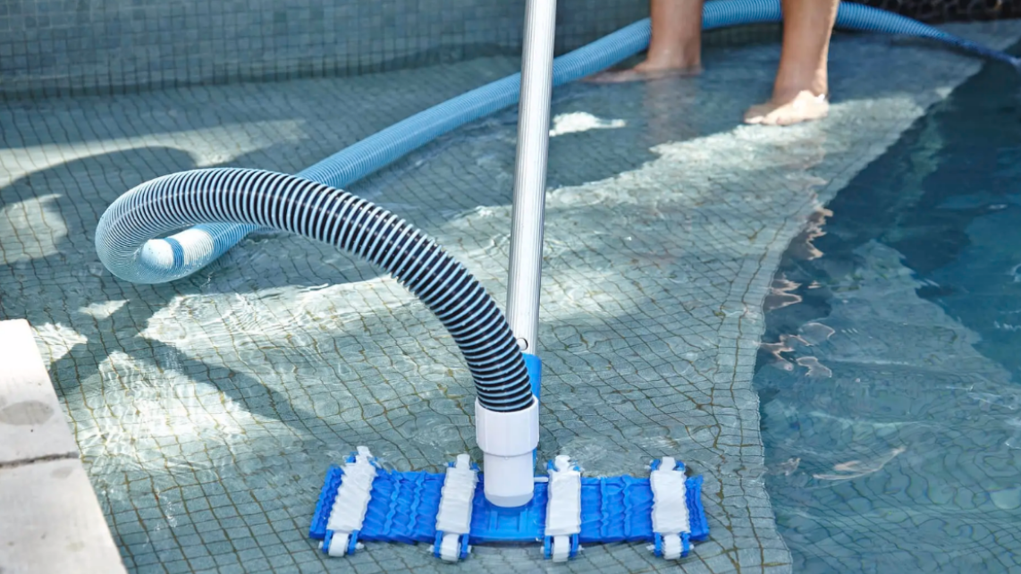 A person using a pool vacuum to clean the pool steps
