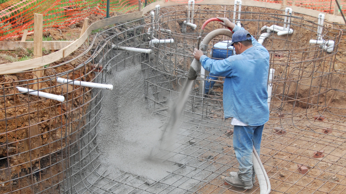 An installer spraying concrete on the shaped and proposed concrete pool, with steel bars already present