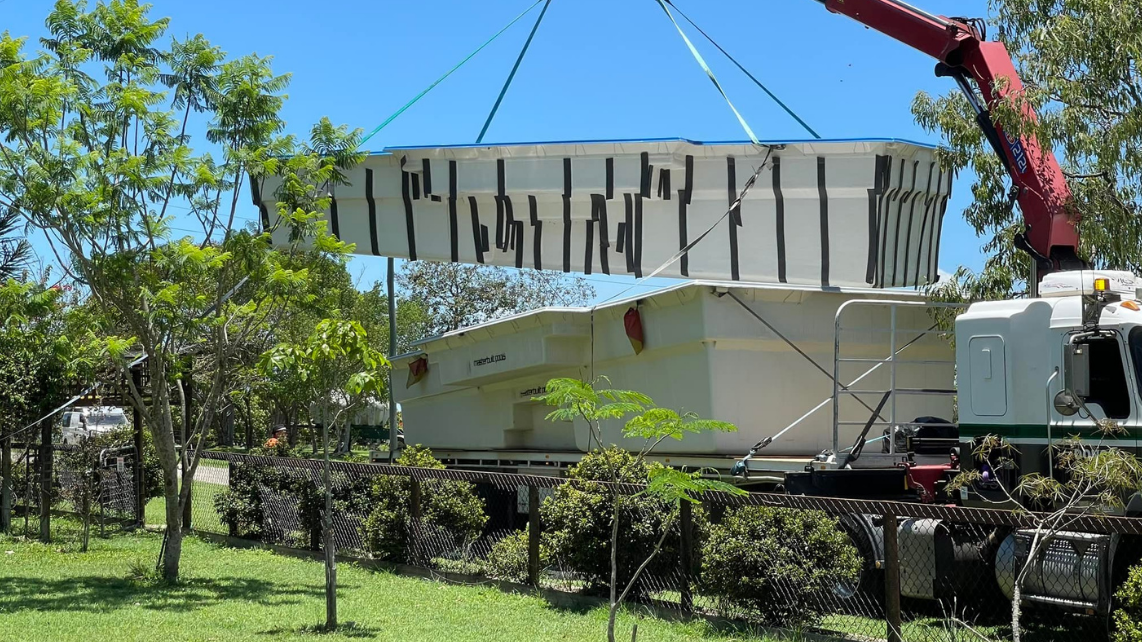 A mobile crane transporting a fibreglass pool shell to site, taken and done by Pool Professionals Mackay